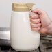 A hand using a Tablecraft 48 oz. dispenser with beige top to pour milk.