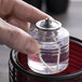 A person's hand holding a Sterno liquid candle fuel cartridge over a glass jar.
