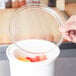 A hand placing a Cambro clear plastic lid over a container of fruit.