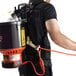 A man wearing a black shirt using a Hoover commercial backpack vacuum cleaner with a hose attached.