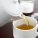 White porcelain teapot pouring tea into a white cup.