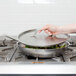 A person's hand using a Vollrath Optio pan lid to cover a pan on a stove.