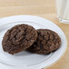 A plate of chocolate cookies next to a glass of milk.