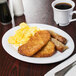 A Diamond White narrow rim oval platter with breakfast food on it on a table with a cup of coffee.