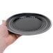 A hand holding a Fineline black plastic plate with a silver rim.