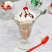 A Libbey tulip sundae glass with chocolate ice cream and whipped cream with a spoon.