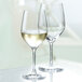 Two Stolzle Bordeaux wine glasses filled with white wine on a table.