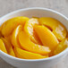 A white bowl of sliced yellow peaches in light syrup.