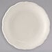 A close-up of a Tuxton Seabreeze eggshell china plate with a scalloped edge on a gray background.