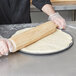 A person rolling out pizza dough on an American Metalcraft Super Perforated Pizza Pan.