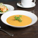 A 10 Strawberry Street gold line porcelain soup bowl filled with soup on a table with a plate of food