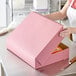 A woman opening a pink Baker's Mark bakery box with a cake inside.