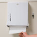 A person's hand pulling a paper towel out of a white San Jamar multi-fold towel dispenser.
