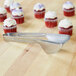 A pair of Carlisle stainless steel pastry tongs next to a cupcake with white frosting.