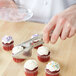 A person using Carlisle stainless steel pastry tongs to pick up a cupcake with white frosting and sprinkles.