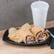 A Dart black laminated foam platter with a tortilla wrap and chips with a cup of milk on a table.