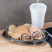 A Dart black laminated foam platter with a sandwich and a drink on a table.