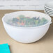 A Fineline white plastic round bowl with a lid on top filled with salad.