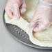 A person in plastic gloves using a Super Perforated Hard Coat Anodized Aluminum wide rim pizza pan to hold dough.