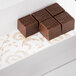 A white glassine pad with gold floral pattern holding chocolate squares.