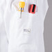 A white Mercer Culinary chef jacket with cloth knot buttons and a pocket with a pen.
