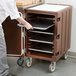 A person putting trays in a brown Cambro cart.