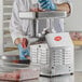 A person in a white coat and blue gloves using an Avantco meat grinder.