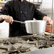 A chef in a uniform uses a Vollrath Wear-Ever sauce pan over a stove.