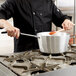 A chef stirring food in a Vollrath Wear-Ever sauce pan on a stove.