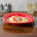 A CAC red square pasta bowl filled with spaghetti with sauce and cheese on a table.