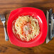 A CAC red square pasta bowl with spaghetti, sauce, and cheese on it with a fork and knife.