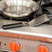 A Mercer Culinary Millennia heavy duty turner next to a pan on a stove.