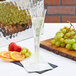 A Fineline Wavetrends clear plastic champagne flute filled with champagne and fruit.