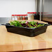 A black melamine food pan with lettuce in it on a counter.