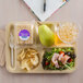 A Carlisle tan plastic 6 compartment tray with food including a sandwich, a pear, and a drink.