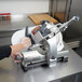 A person using a Hobart meat slicer to cut meat.