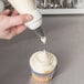 A hand using an Ateco plastic coupler on a pastry bag to frost a cupcake.