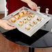 A hand holding a Vollrath stainless steel serving tray of sushi rolls.