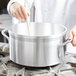 A person stirring a Vollrath Wear-Ever Classic Select aluminum sauce pot with a wooden spoon.