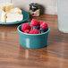 A Fiesta turquoise china ramekin filled with raspberries and blueberries on a table.