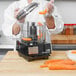 A person in a white coat using a Waring food processor to chop carrots.