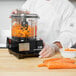 A chef in a white coat using a Waring food processor to chop carrots on a counter.