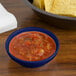 A cobalt blue melamine salsa dish filled with salsa on a table with a bowl of chips.