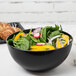 A Fineline black plastic bowl filled with salad and croissants on a table.