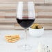 A close up of a Chef & Sommelier tall wine glass filled with red wine next to crackers and green olives.