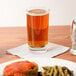 A Libbey highball glass filled with beer on a table next to a plate of food.