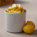 A white Cal-Mil melamine bowl filled with lemon wedges and a lemon slice on a counter.