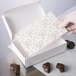 A hand placing a white and gold floral pad in a white candy box.