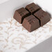 A white 3-ply glassine pad with gold floral pattern holding three chocolate bars.