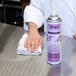 A person cleaning a stainless steel counter with Noble Chemical Excel Stainless Steel Cleaner using a white cloth.